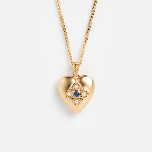 Rose’s Blue Sapphire Heart Locket is a gold vermeil heart locket necklace with a cluster of blue sapphires in a floral pattern at the center, shown on a simple gold chain against a plain white background.