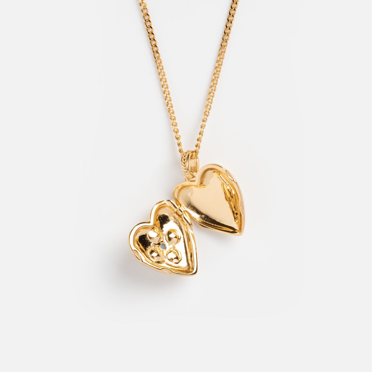 Rose’s Blue Sapphire Heart Locket rests on a plain white background, its gold vermeil heart shape slightly open to reveal space inside for tiny photos or keepsakes.