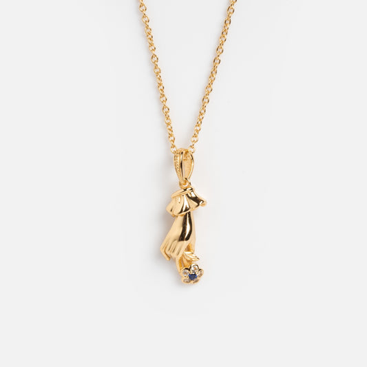 The Forget Me Not Blue Topaz Memento Necklace is a gold vermeil piece with a dog head and paw pendant holding a round blue topaz gemstone, inspired by vintage designs and shown on a white background.