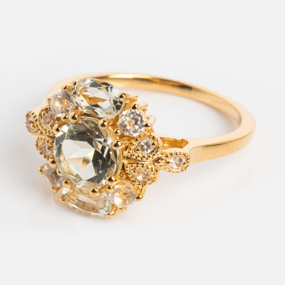 The Royal Gardens Green Amethyst Cocktail Ring showcases a large, oval-cut green amethyst accented by smaller round stones in an ornate, vintage-inspired 14k Gold Vermeil setting, displayed on a plain white background.