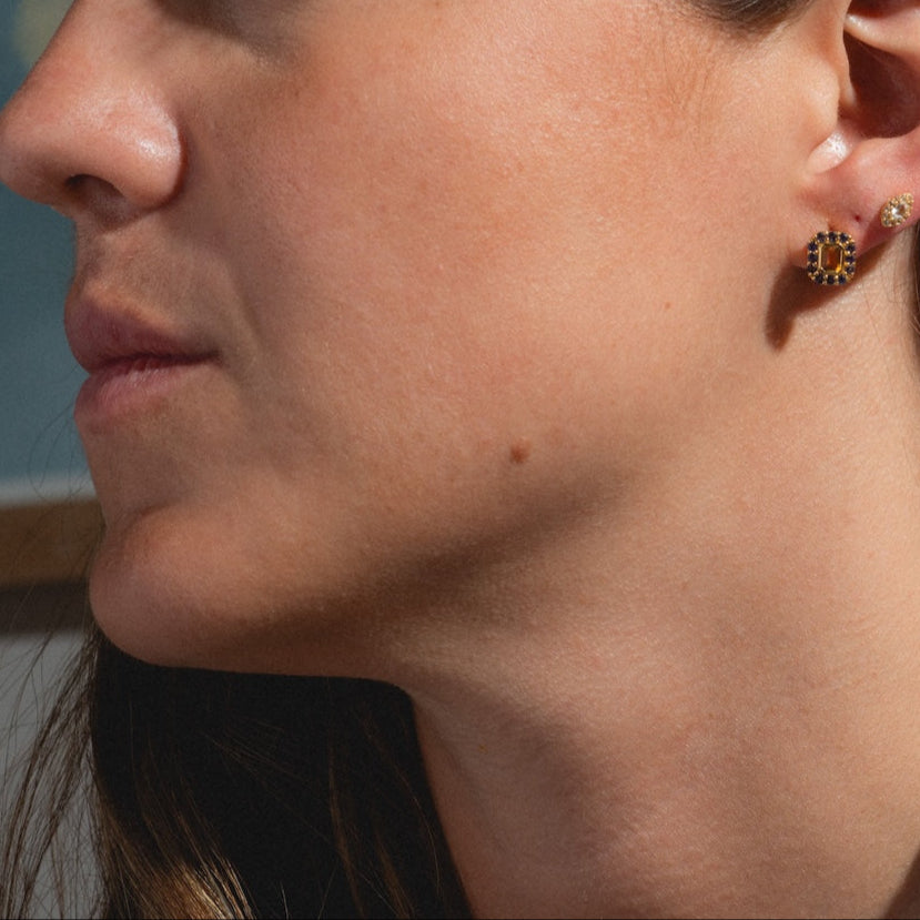 Close-up of a woman in profile, highlighting her jawline, lips, and ear. She wears Citrine and Iolite Novella Studs and a larger round gold vermeil earring with a decorative pattern. Her long brown hair is also visible.