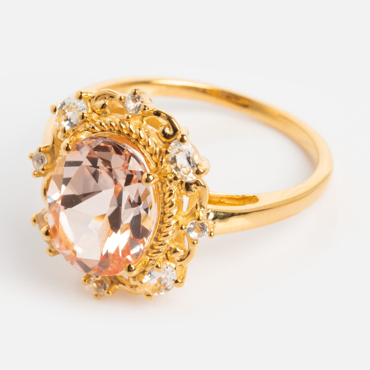 The Royal Blush Cocktail Ring features a large oval pale pink gemstone in an ornate 14k gold vermeil setting, accented by smaller clear stones, and is shown against a plain white background.