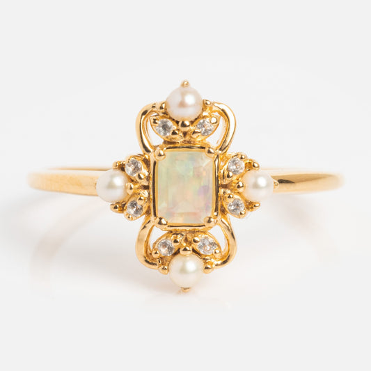 The Crown Jewel Opal and Pearl Ring is a 14k gold vermeil piece with a rectangular opal center, framed by pearls and diamonds in an ornate, vintage-inspired setting, shown against a plain white background.