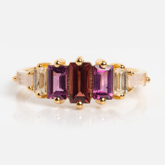 The Berry Baroque Garnet Crown Ring is a gold vermeil Art Deco ring with five rectangular gemstones in a row: clear stones on the ends, purple stones beside them, and a garnet centerpiece, all set with gold prongs on a simple band.