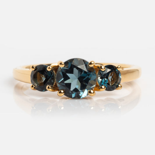 The London Blue Topaz Trilogy Ring features a vintage-inspired gold design with an oval-cut center stone and two smaller round gems, all set against a plain white background.