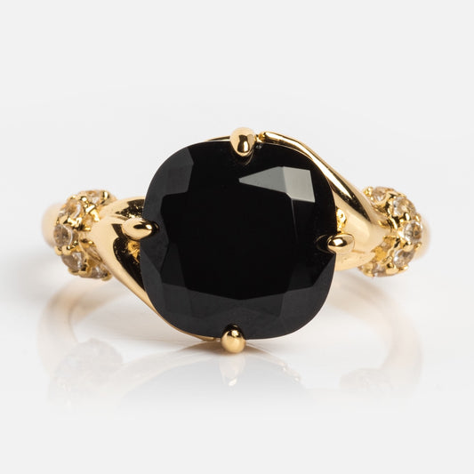 The Past Life Black Spinel Statement Ring features a vintage-inspired gold design with a large faceted black spinel at the center, intricate detailing, and small clear stones accenting the band.
