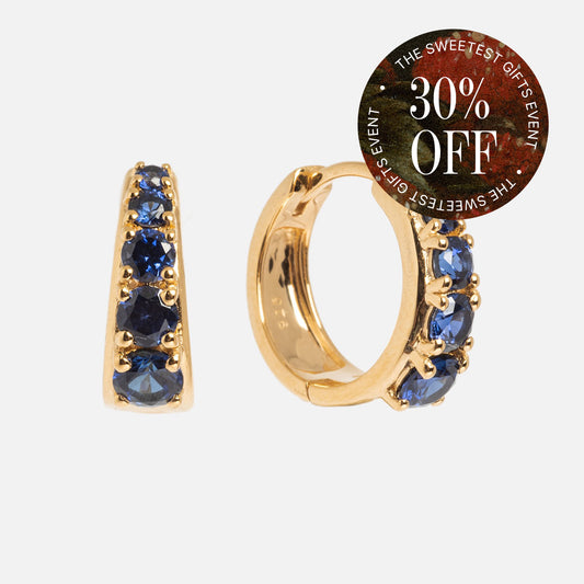 Sapphire Soliloquy Huggie Hoops: Gold vermeil earrings with a row of blue sapphires. A circular label in the top right corner says, "30% OFF THE SWEETEST GIFTS EVENT.