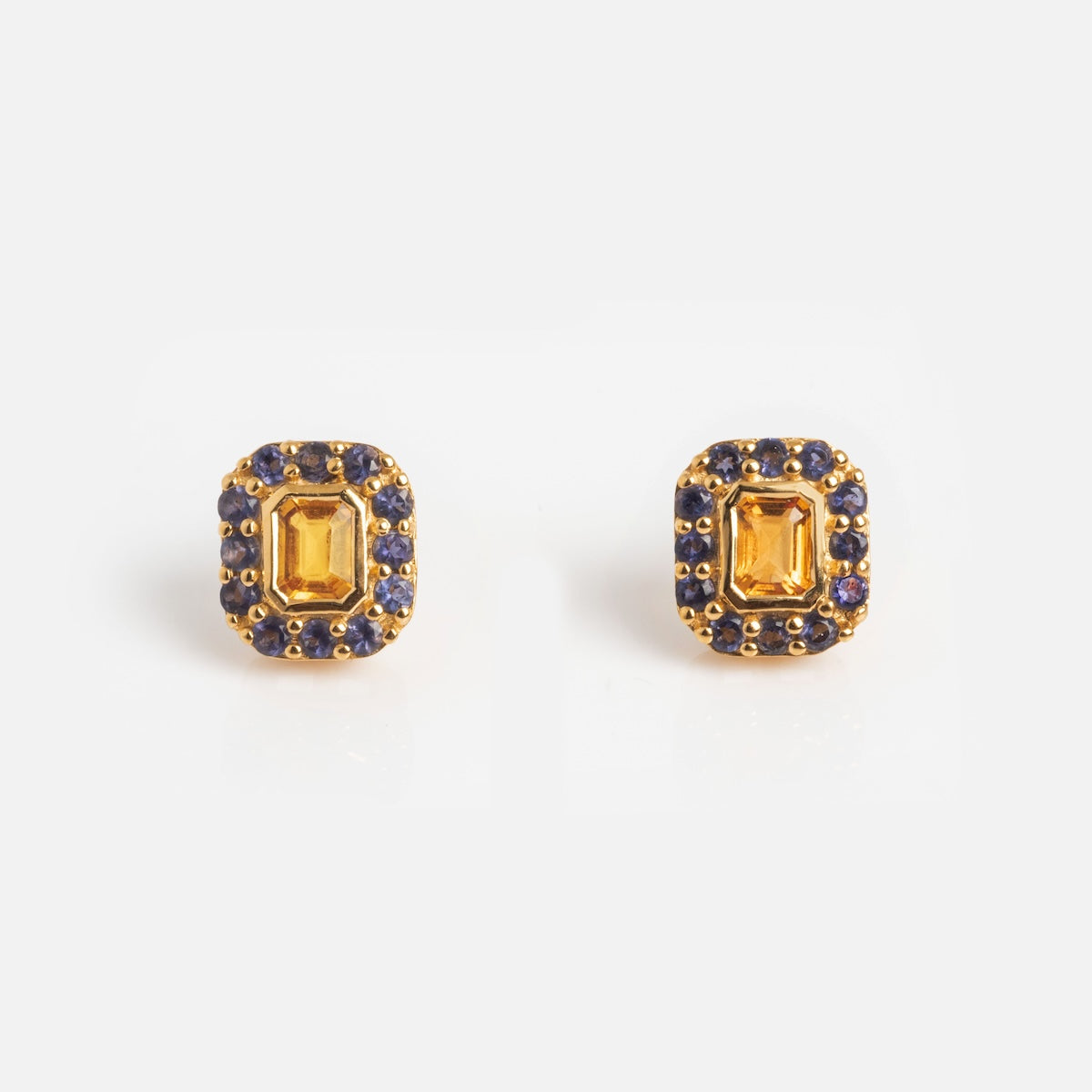 The Citrine and Iolite Novella Studs feature gold vermeil rectangular studs with a central yellow citrine gemstone, surrounded by small blue iolite stones—an elegant accessory for any occasion.