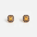 The Citrine and Iolite Novella Studs feature gold vermeil rectangular studs with a central yellow citrine gemstone, surrounded by small blue iolite stones—an elegant accessory for any occasion.
