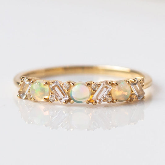 The 14k Australian Opal and Baguette White Sapphire Ring (Sample Size 7) features three round opals and four baguette-cut white sapphires set in recycled yellow gold, elegantly displayed on a white reflective surface.