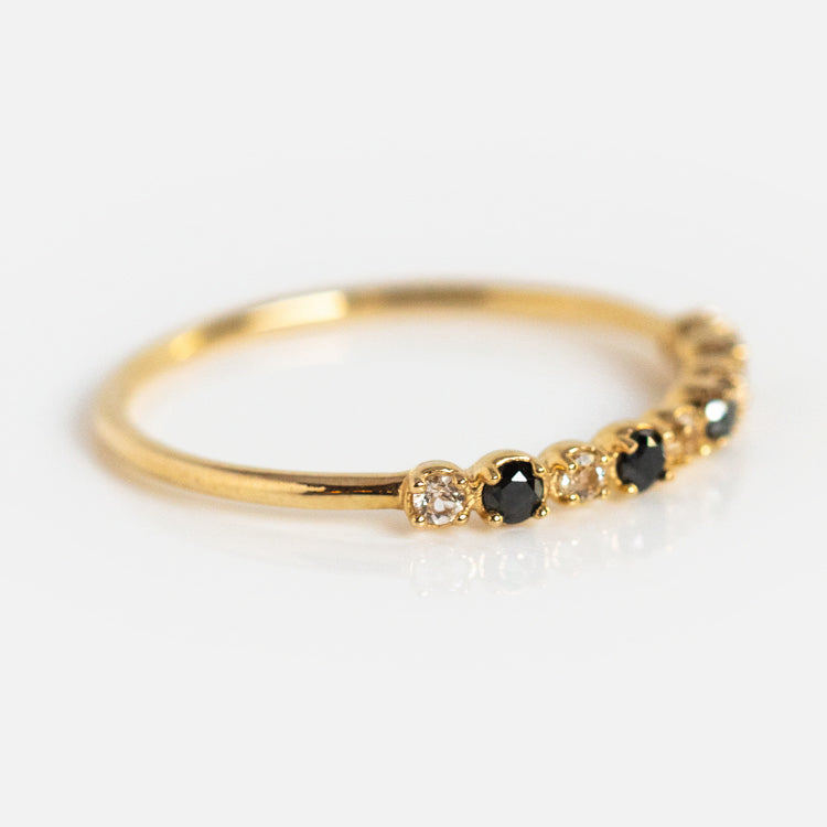 The 14k Classic White Sapphire and Black Diamond Band features alternating black diamonds and white sapphires set in a row on a yellow gold band, displayed against a white background.