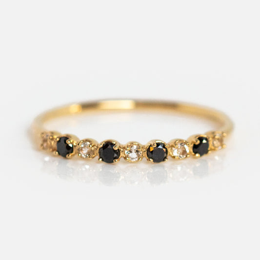 The 14k Classic White Sapphire and Black Diamond Band features alternating black diamonds and white sapphires set in a delicate yellow gold band, shown against a white background.