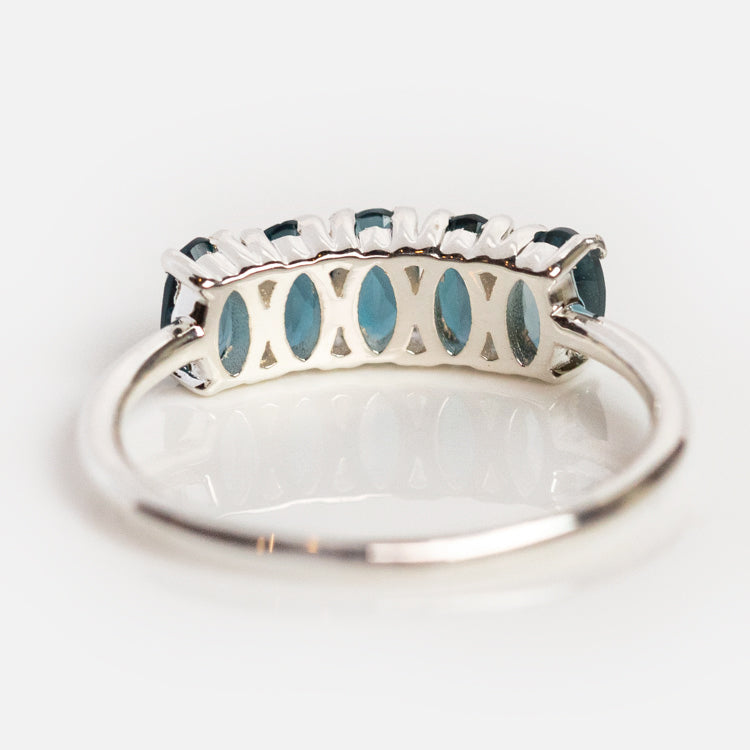 The London Blue Topaz Galaxy Ring in Silver features oval blue topaz gemstones set in a row with crisscross lattice detailing on the band, enhancing its brilliance. Shown on a white background.