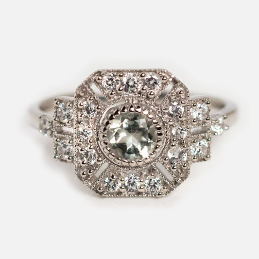 The Venus Ring is a vintage-style sterling silver statement piece with a round central gemstone, accented by smaller sparkling stones in an ornate geometric setting.