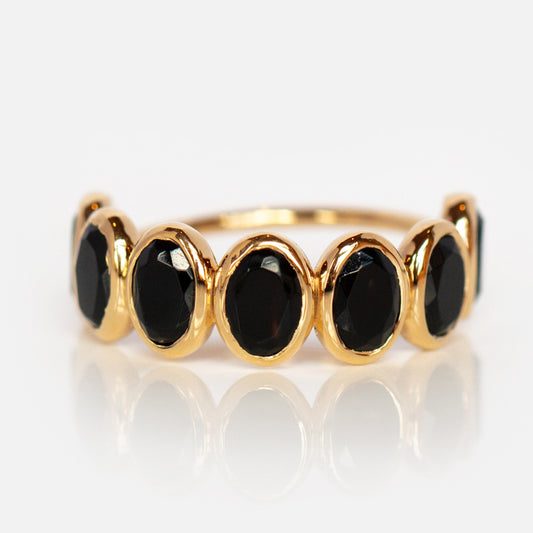 The Violeta Black Onyx Ring showcases seven oval black onyx gemstones set in a row within smooth 14k yellow gold vermeil bezels, displayed against a white background.