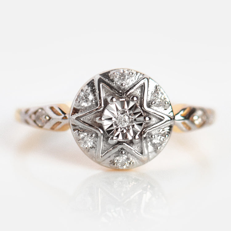 The Vintage Star Compass Ring features a round, star-shaped setting with a central diamond, smaller diamonds, detailed band engraving, and is crafted in sterling silver with 14k yellow gold plating.
