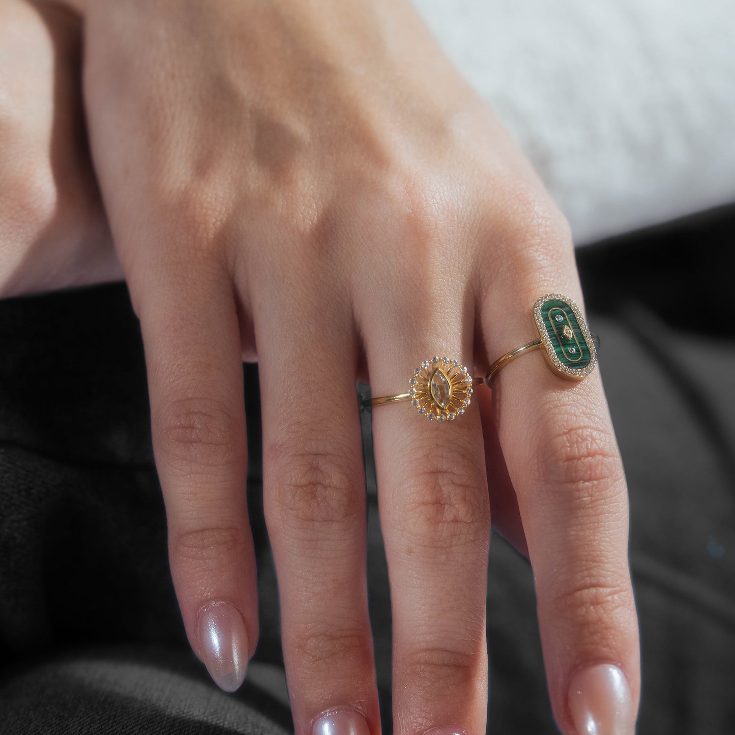 A close-up of a hand with natural nails, wearing two gold rings—one featuring the So Art Deco Cocktail Ring with an oval green malachite stone set in 14k yellow gold vermeil and intricate designs.