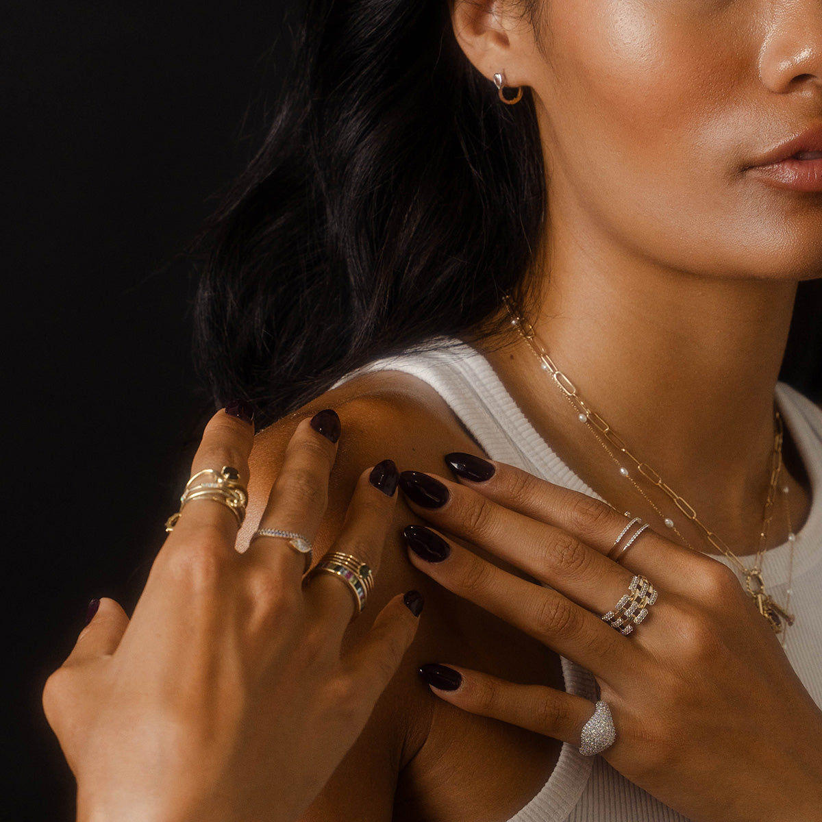 A woman in a white tank top showcases the Solid Gold Mirrored Light Diamond Statement Ring on her finger, along with gold necklaces and dark nail polish. Her face is partially visible as she poses against a black background.