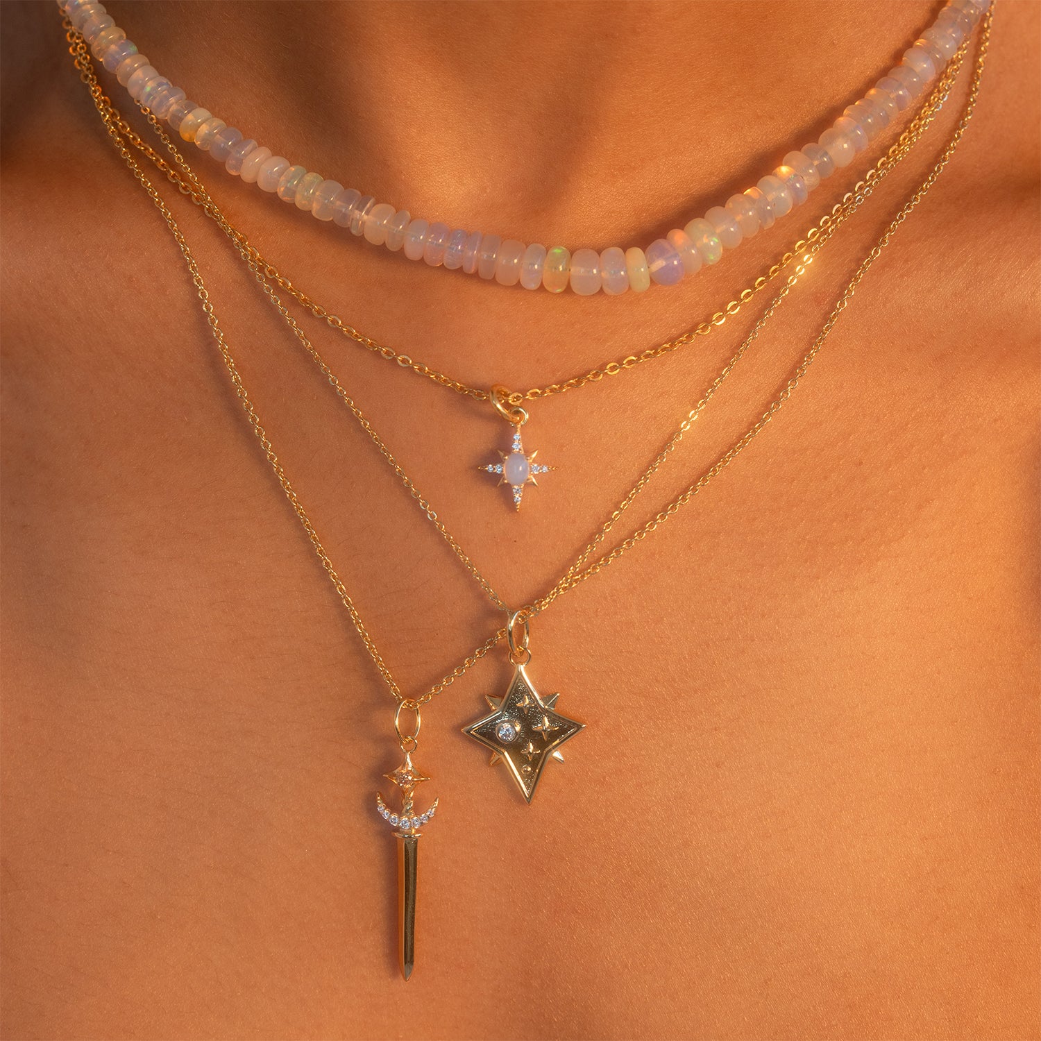 Close-up of a person wearing the Sabrina Opal Portal Necklace layered with a beaded choker and gold chains adorned with star and spike pendants, set against sun-kissed skin.