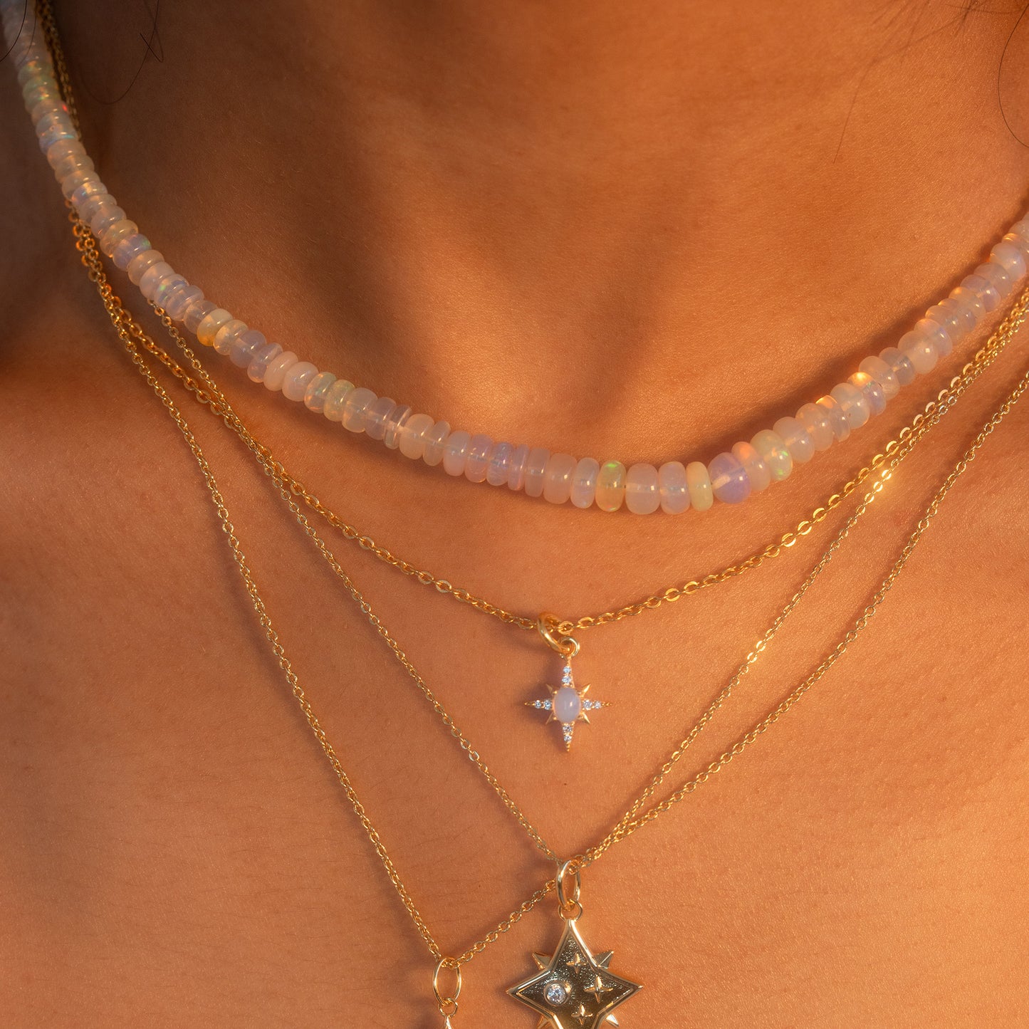 Close-up of a person wearing a Beaded Gemstone Necklace as a choker, layered with two 18k gold plated necklaces featuring star-shaped pendants, set against warm, sunlit skin.