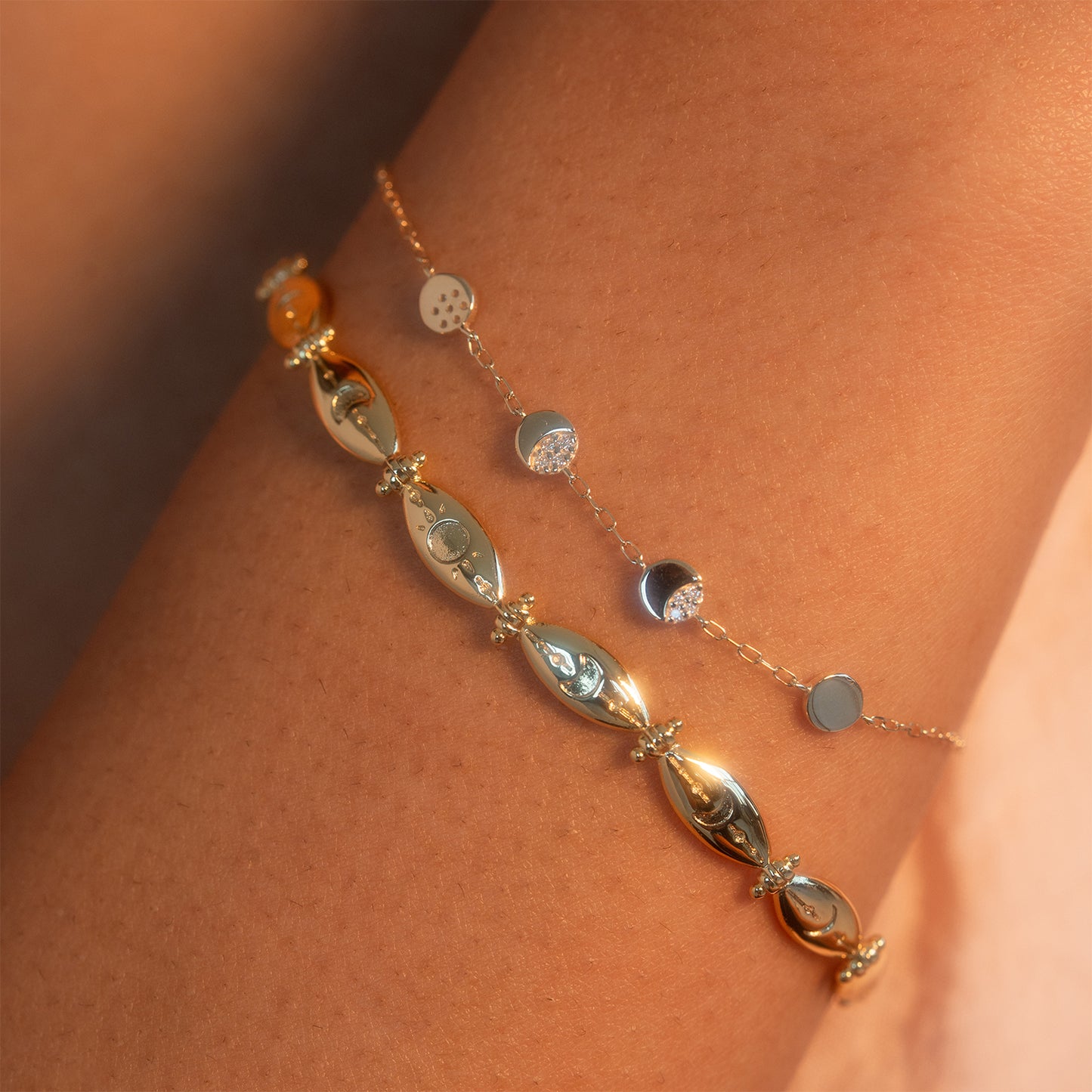 Close-up of the Midnight Moon Phases Bracelet: a delicate gold chain with small round disc charms on a person's wrist, highlighted by warm, soft lighting that accentuates its shine.
