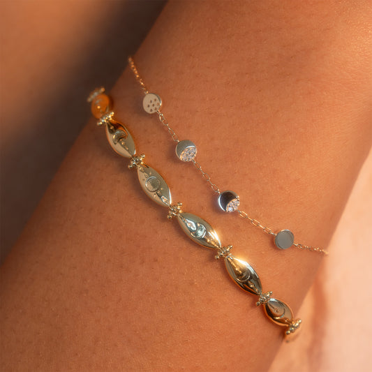 Close-up of the Midnight Moon Phases Bracelet: a delicate gold chain with small round disc charms on a person's wrist, highlighted by warm, soft lighting that accentuates its shine.