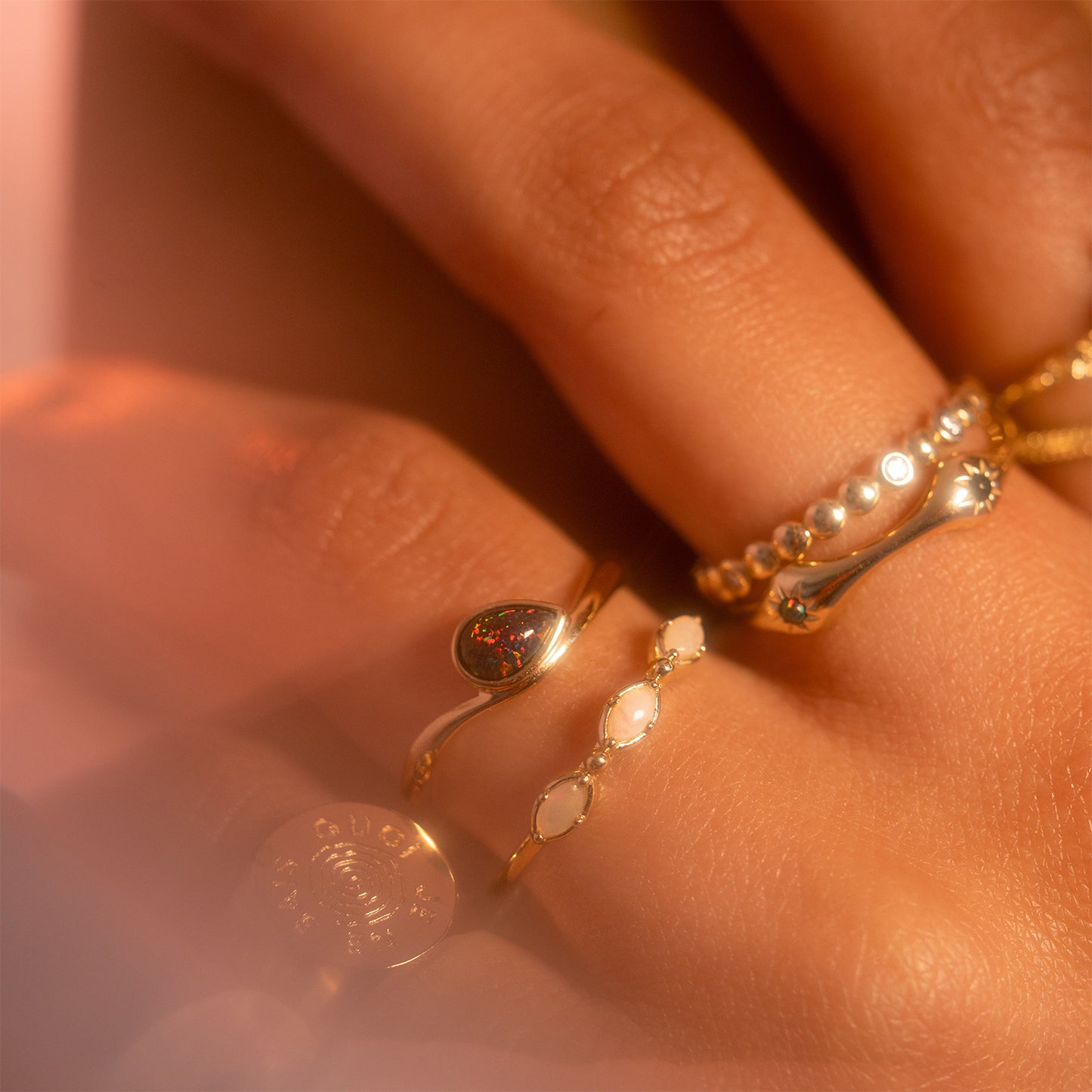 A close-up of a hand wearing the Solid Gold Black Opal Galaxy Droplet Ring, featuring opal details and engraved gold, on softly lit fingers.