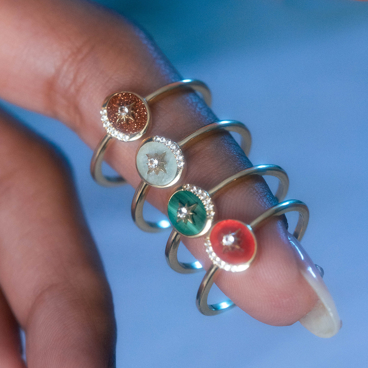 A hand with long, manicured nails wears the Solid Gold Crystal Crescent Moon Ring for Manifestation, featuring a circular colorful enamel setting and a central gemstone inspired by natural crystals.