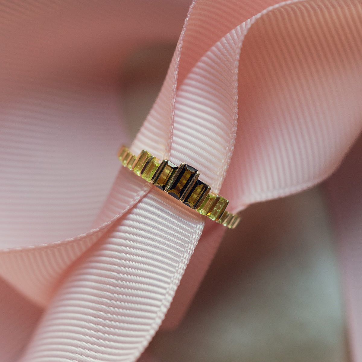 The 10k Green Tourmaline Skyline Band, featuring rectangular dark stones, is displayed on a pale pink textured ribbon.