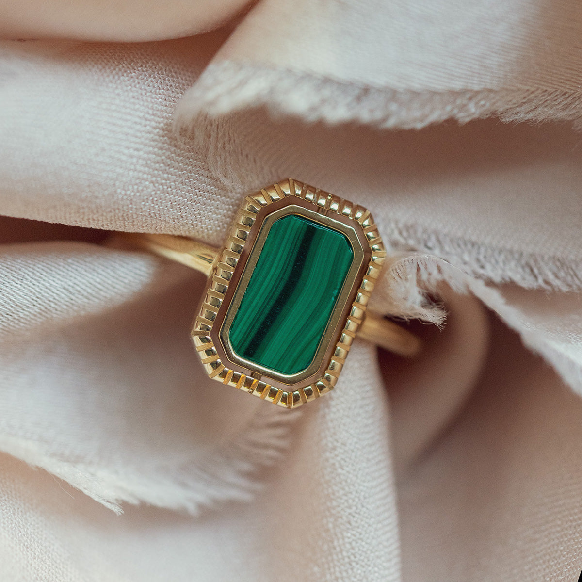 The 10k Gallery Frames Enamel and Malachite Reversible Ring features a rectangular green malachite stone with dark stripes, displayed on a soft pale pink fabric background.