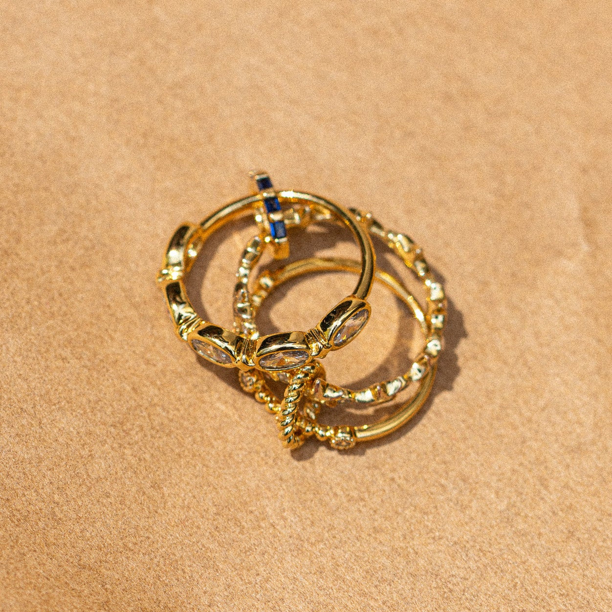Gold hoop earrings with embedded stones on a beige fabric background