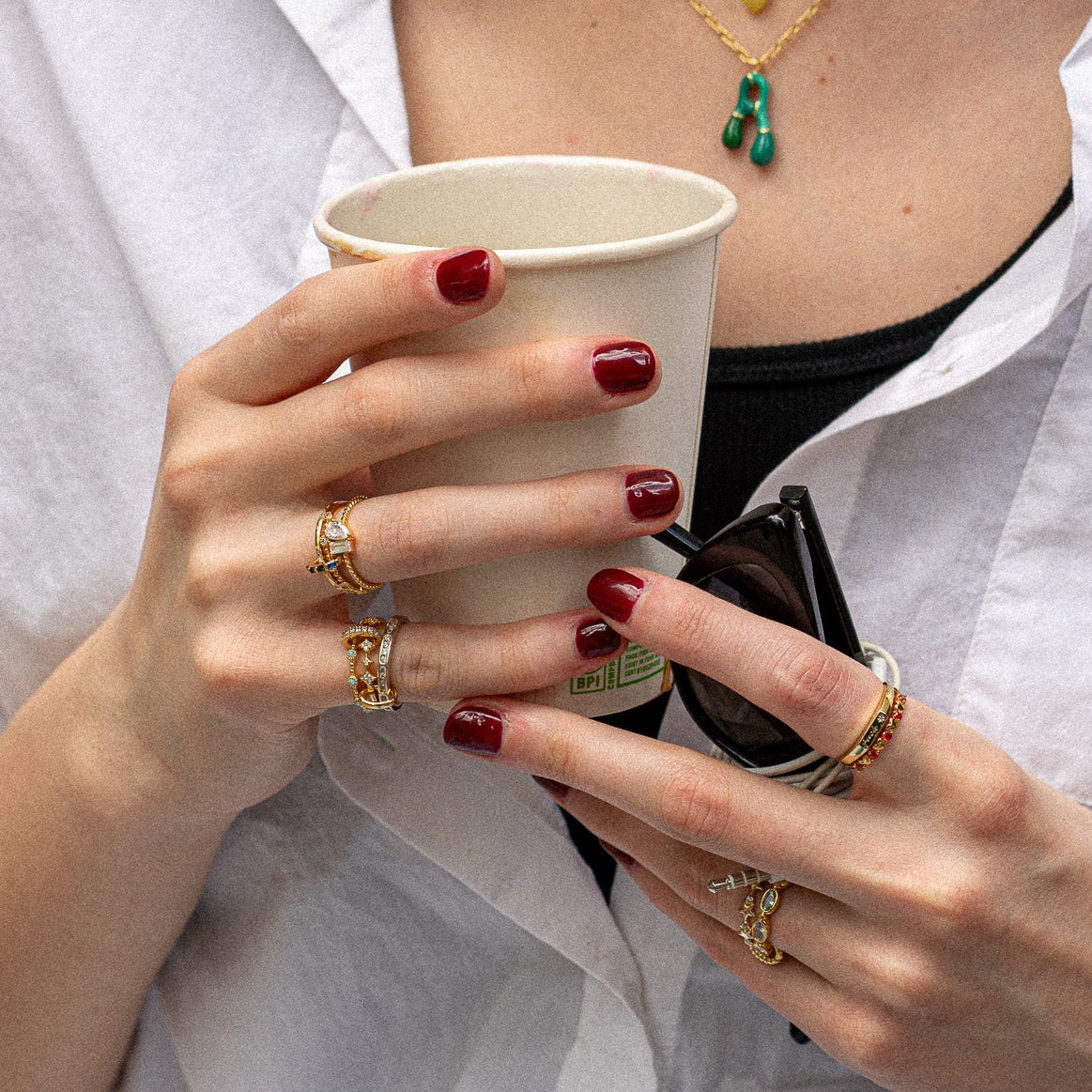 Person holding a coffee cup with jewelry on, wearing a white shirt.