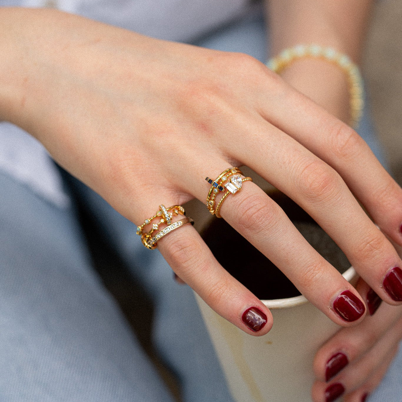 Close-up of a hand with multiple gold rings holding a white mug.