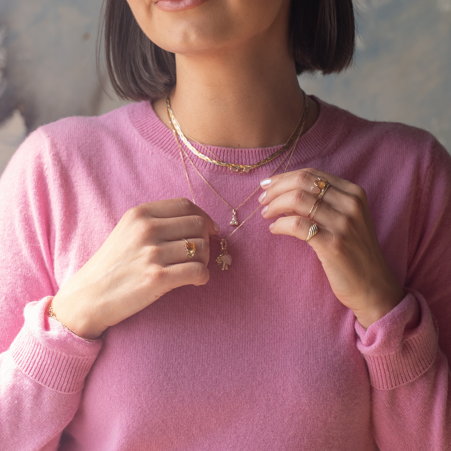 A woman wearing a pink sweater and the Solid Gold Morning Light Citrine and Sunstone Necklace that adds a touch of elegance.
