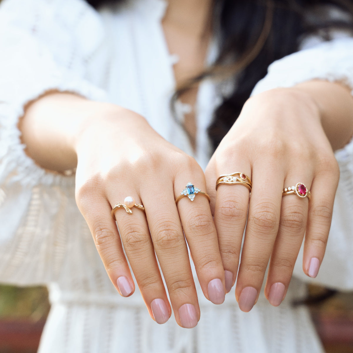 A person with long dark hair and a white textured top shows both hands, highlighting the 10k Hidden Message Morse Code Diamond Band on their manicured fingers with light pink polish.