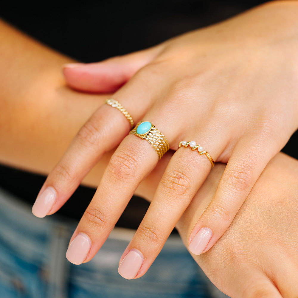 A close-up shows two manicured hands, one wearing the Solid Gold Mesh Gemstone Ring with turquoise (sample size 7), alongside a pearl band and gold mesh ring, resting gently together against a softly blurred background.