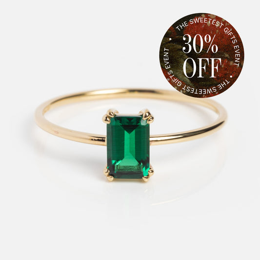 A Solid Gold Essential Baguette Birthstone Ring with a rectangular green gemstone is shown on a white background. A round sticker in the corner says “30% OFF - THE SWEETEST GIFTS EVENT” in white text on a red and black background.