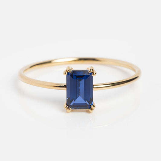 The Solid Gold Essential Baguette Birthstone Ring Blue Sapphire Sample showcases an emerald-cut deep blue sapphire on a slim yellow gold band with a minimalist four-prong setting, set against a plain white background.