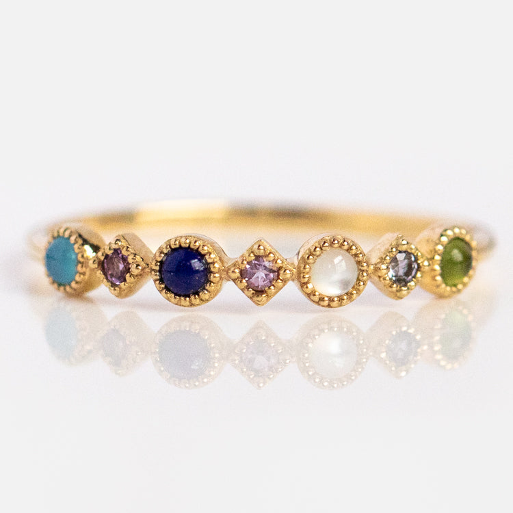 The Solid Gold Balance Acrostic Ring, Sample Size 7, is crafted in 9k yellow gold and showcases small round and diamond-shaped multicolored gemstones—such as blue chalcedony and amethyst—set in a row.