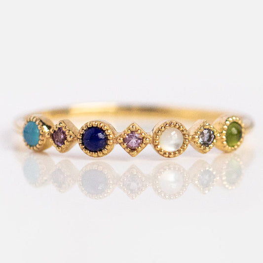 The Solid Gold Balance Acrostic Ring, Sample Size 7, is crafted in 9k yellow gold and showcases small round and diamond-shaped multicolored gemstones—such as blue chalcedony and amethyst—set in a row.