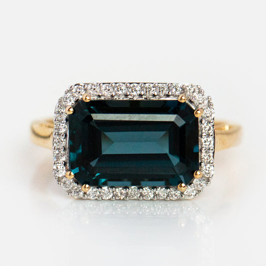 The 14k Solid Gold Diamond East West Baguette Ring features a large rectangular London blue topaz centerpiece, beautifully accented with a halo of sparkling diamonds.