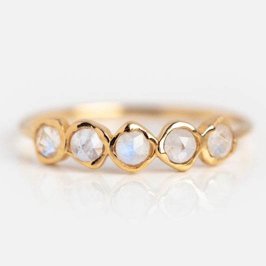 The Solid Gold Organic Moonstone Ring features five bezel-set round blue moonstones with a translucent, iridescent look, arranged in a row on a plain gold band, displayed against a white background.