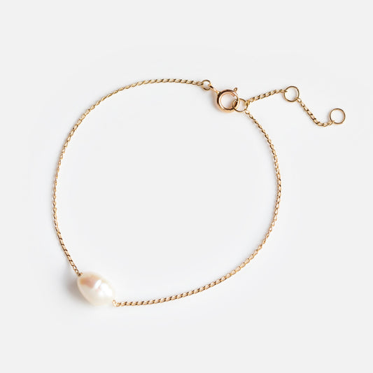 The Solid Gold Single Pearl Chain Bracelet features a delicate gold chain, a single freshwater pearl, and an adjustable clasp—ideal for bridal jewelry—shown on a white background.