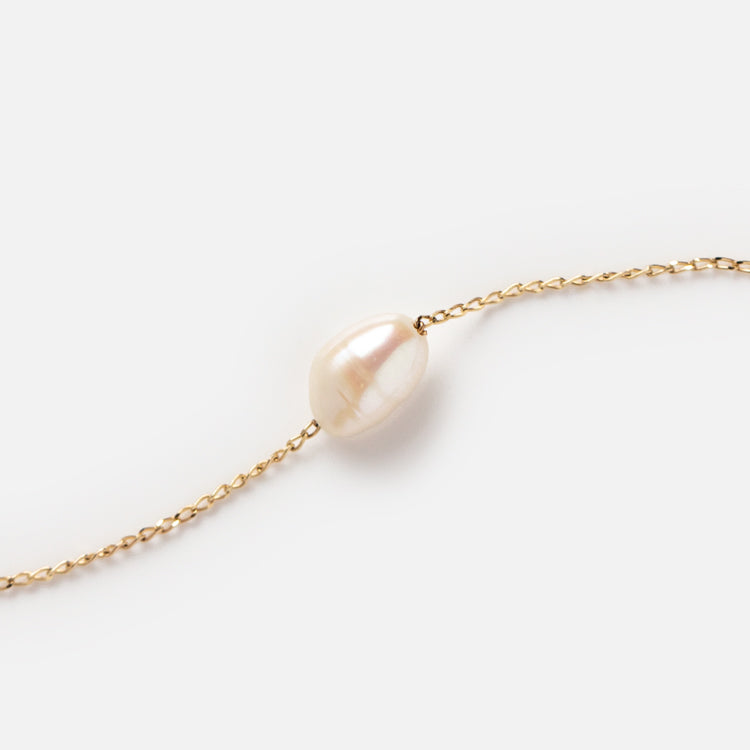 A delicate Solid Gold Single Pearl Chain Bracelet featuring a single, oval-shaped freshwater pearl as its centerpiece, showcased on a plain white background—an elegant and timeless accessory.