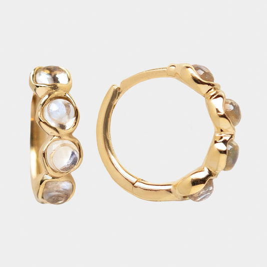 The Solid Gold Organic Moonstone Huggies Sample features a pair of 9k yellow gold hoops, each set with three round blue moonstones. Shown against a plain white background, one earring displays the front view and the other the side.