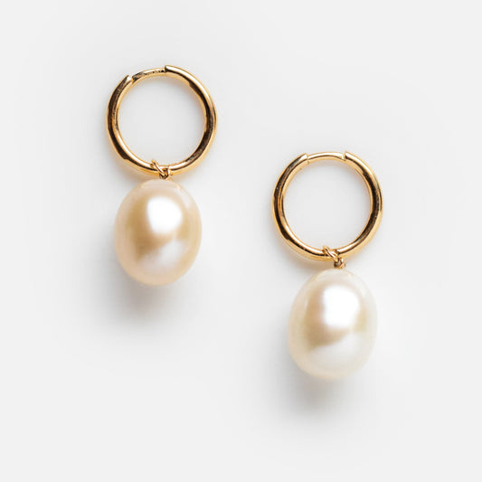 The Solid Gold Elegant Pearl Charm Huggies are shown on a plain white background, featuring gold hoops with a single freshwater pearl drop on each earring.