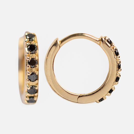 The Solid Gold Black Diamond Huggie Hoops Sample features small 10k yellow gold hoops with embedded black diamonds, displayed from side and front views against a plain white background.