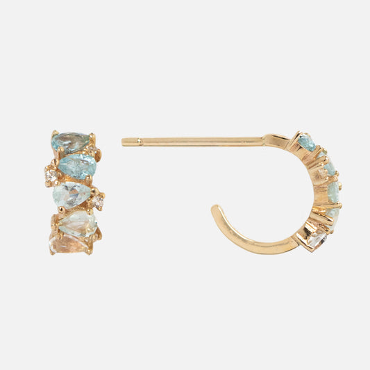 Solid Gold Ombre Birthstone Huggie Hoops feature blue and clear gemstones set along the outer edge, shown from the side and front on a plain white background. These 9k gold earrings make a stunning choice for any occasion.