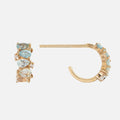 Solid Gold Ombre Birthstone Huggie Hoops feature blue and clear gemstones set along the outer edge, shown from the side and front on a plain white background. These 9k gold earrings make a stunning choice for any occasion.