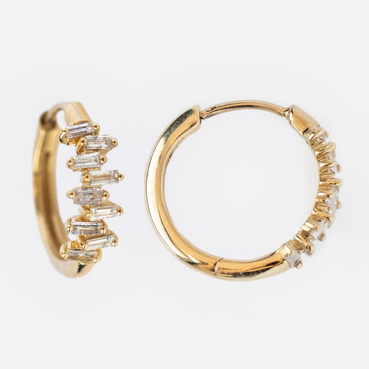 The Solid Gold Diamond Baguette Huggie Hoops are geometric earrings in gold, each featuring a row of small rectangular diamonds on the front half, shown against a white background.